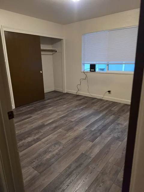 Unfurnished bedroom with wood-look plank flooring, a partially open closet, and a window with blinds.